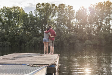 Young couple embracing on jetty at a remote lake - UUF17934