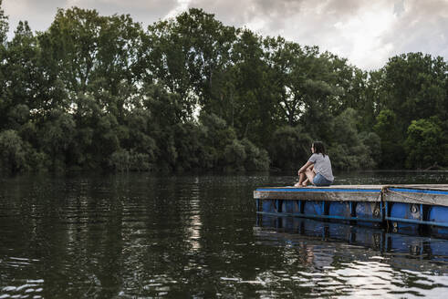 Relaxed woman sitting on jetty at a remote lake - UUF17941