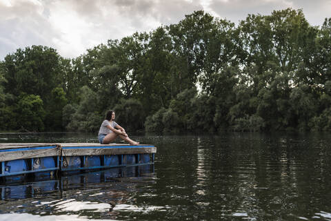 Relaxed woman sitting on jetty at a remote lake stock photo