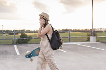 Junge Frau mit Mobiltelefon und Longboard auf dem Parkdeck - UUF17949