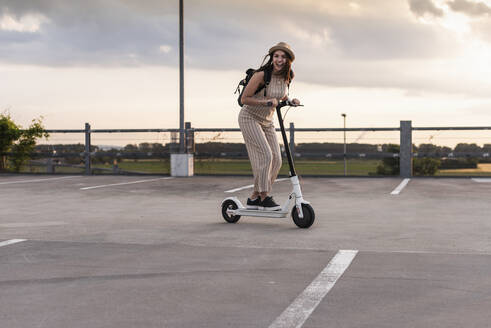 Glückliche junge Frau auf Elektroroller auf Parkdeck - UUF17969