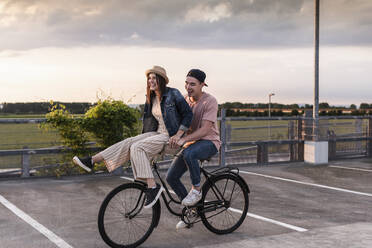 Glückliches junges Paar zusammen auf einem Fahrrad auf einem Parkdeck - UUF17971