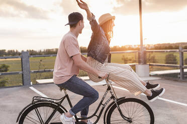 Happy young couple together on a bicycle on parking deck at sunset - UUF17972