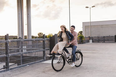 Glückliches junges Paar zusammen auf einem Fahrrad auf einem Parkdeck - UUF17973