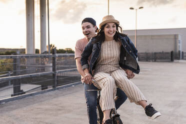 Glückliches junges Paar zusammen auf einem Fahrrad auf einem Parkdeck - UUF17976