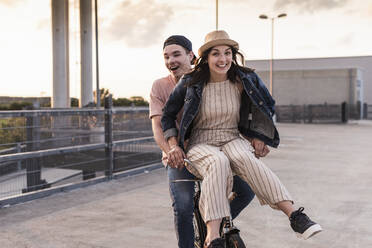 Happy young couple together on a bicycle on parking deck - UUF17976