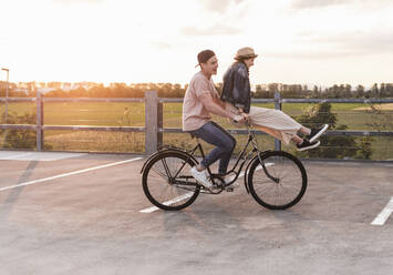 Happy young couple together on a bicycle on parking deck at sunset - UUF17978