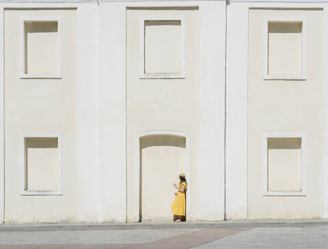 Seitenansicht einer Frau, die ein Mobiltelefon benutzt, während sie an einem Gebäude in der Stadt steht, lizenzfreies Stockfoto