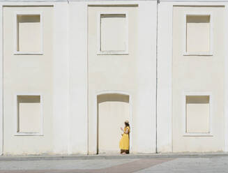 Side view of woman using mobile phone while standing by building in city - AHSF00570