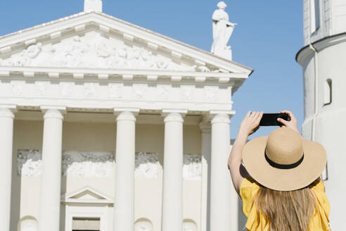 Rückansicht einer Frau, die mit ihrem Smartphone eine Kathedrale in der Stadt an einem sonnigen Tag fotografiert - AHSF00581