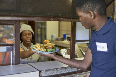 Junger Kellner nimmt geliefertes Essen aus der Restaurantküche, Südafrika - VEGF00334