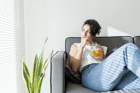 Entspannte junge Frau auf der Couch sitzend mit einem Softdrink, lizenzfreies Stockfoto
