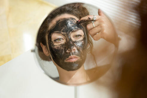 Spiegelbild einer jungen Frau, die zu Hause eine Gesichtsmaske aufträgt - JPTF00235