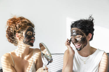 Zwei glückliche junge Frauen, die zu Hause Gesichtsmasken auftragen - JPTF00242