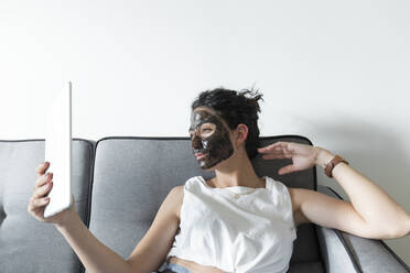 Young woman wearing facial mask and using tablet at home - JPTF00243