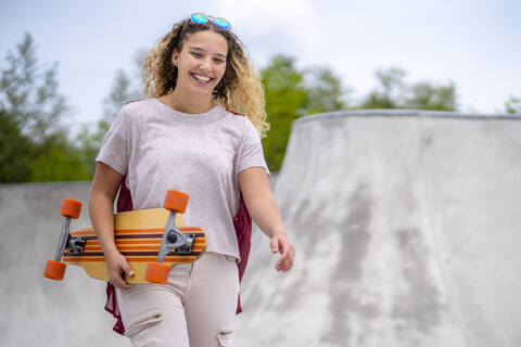 Lächelnde junge Frau mit einem Longboard in einem Skatepark, lizenzfreies Stockfoto