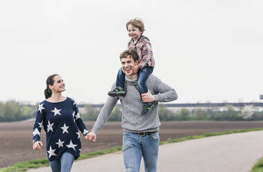 Glückliche Familie, die gemeinsam neben den Feldern spazieren geht, der Vater trägt den Sohn Huckepack - UUF17985