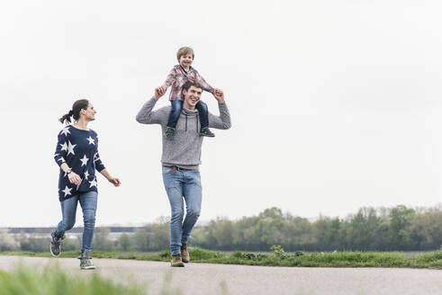 Glückliche Familie, die gemeinsam neben den Feldern spazieren geht, der Vater trägt den Sohn Huckepack - UUF17987