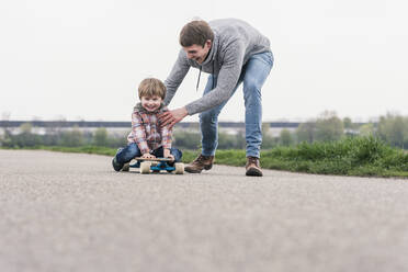 Vater und Sohn haben Spaß, spielen mit Skateboard im Freien - UUF17996