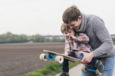 Father and son having fun, playing with skateboard outdoors - UUF17998