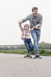 Father and son having fun, playing with skateboard outdoors - UUF18000