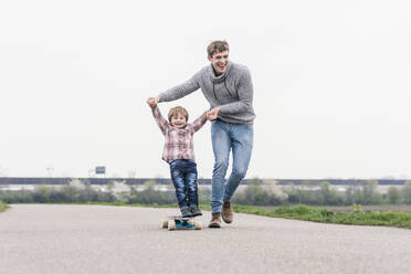 Father and son having fun, playing with skateboard outdoors - UUF18002