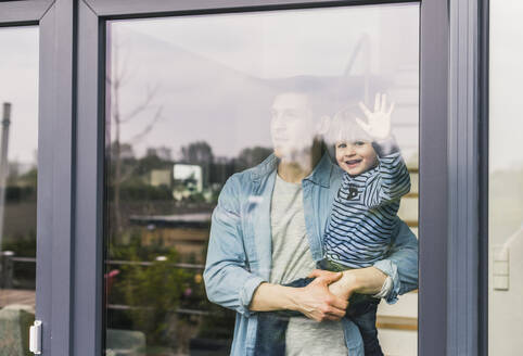 Father holding laughing son, looking out of window - UUF18005