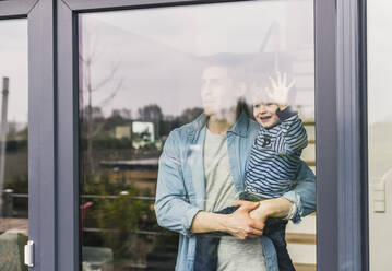 Father holding laughing son, looking out of window - UUF18006