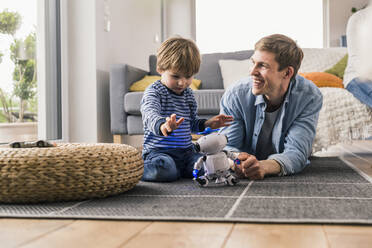 Vater und Sohn liegen auf dem Boden und spielen mit einem Spielzeugroboter - UUF18009