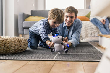 Vater und Sohn liegen auf dem Boden und spielen mit einem Spielzeugroboter - UUF18010