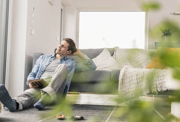 Mid adult man sitting on floor, using digital tablet - UUF18013