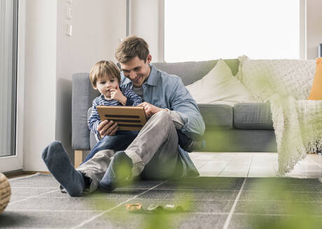 Vater und Sohn sitzen auf dem Boden und benutzen ein digitales Tablet - UUF18015