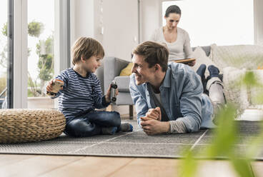 Father and son playing with toy cars, lying on floor - UUF18017