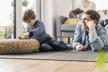 Father and son playing with toy cars, lying on floor - UUF18018