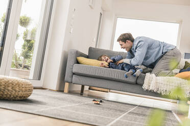 Vater spielt mit seinem Sohn, der auf der Couch liegt - UUF18020