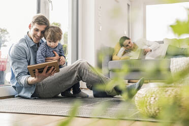 Vater und Sohn liegen auf dem Boden und benutzen ein digitales Tablet - UUF18022