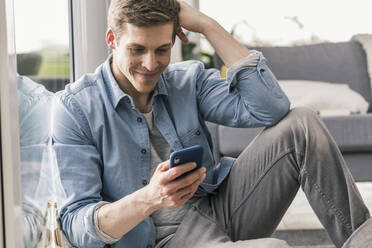 Mittlerer erwachsener Mann am Fenster sitzend, Smartphone benutzend - UUF18025