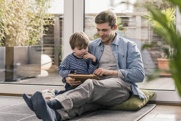Vater und Sohn sitzen auf dem Boden und benutzen ein digitales Tablet - UUF18027