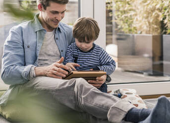 Father and son sitting on floor, using digital tablet - UUF18028