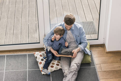 Vater und Sohn sitzen auf dem Boden und benutzen ein digitales Tablet - UUF18029