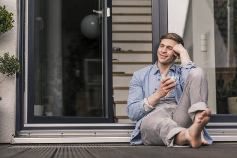 Lächelnder Mann, der eine Pause macht und vor seinem Haus Kaffee trinkt, lizenzfreies Stockfoto