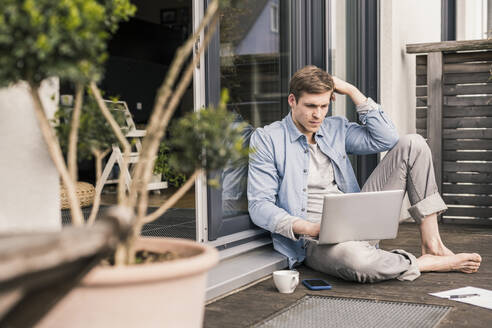 Mann sitzt auf einer Terrasse und benutzt einen Laptop - UUF18037
