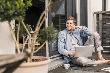 Mann sitzt auf einer Terrasse und benutzt einen Laptop - UUF18038