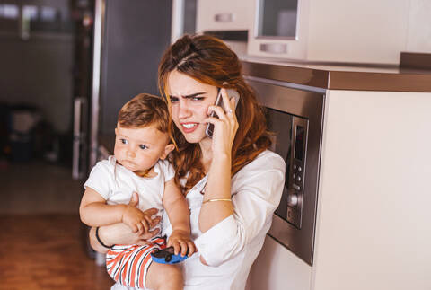 Verärgerte Mutter mit ihrem Sohn, der zu Hause telefoniert, lizenzfreies Stockfoto