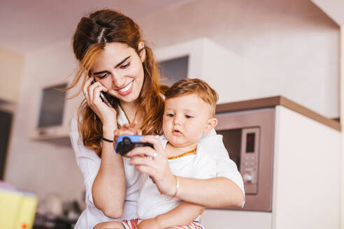 Glückliche Mutter mit ihrem Sohn beim Telefonieren zu Hause - LJF00267