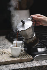 Cropped hand of mature woman pouring coffee in cup on kitchen counter at home - ALBF00877