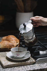 Cropped hand of mature woman pouring coffee in cup on kitchen counter at home - ALBF00879