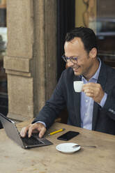 Lächelnder Geschäftsmann bei der Arbeit in einem Kaffeehaus - ALBF00888