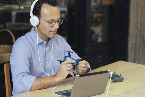 Businessman with headphones, laptop and drone in a coffee shop - ALBF00890