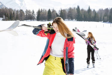 Zwei jugendliche Skifahrerinnen gehen in einer verschneiten Landschaft spazieren, Tirol, Steiermark, Österreich - CUF51634